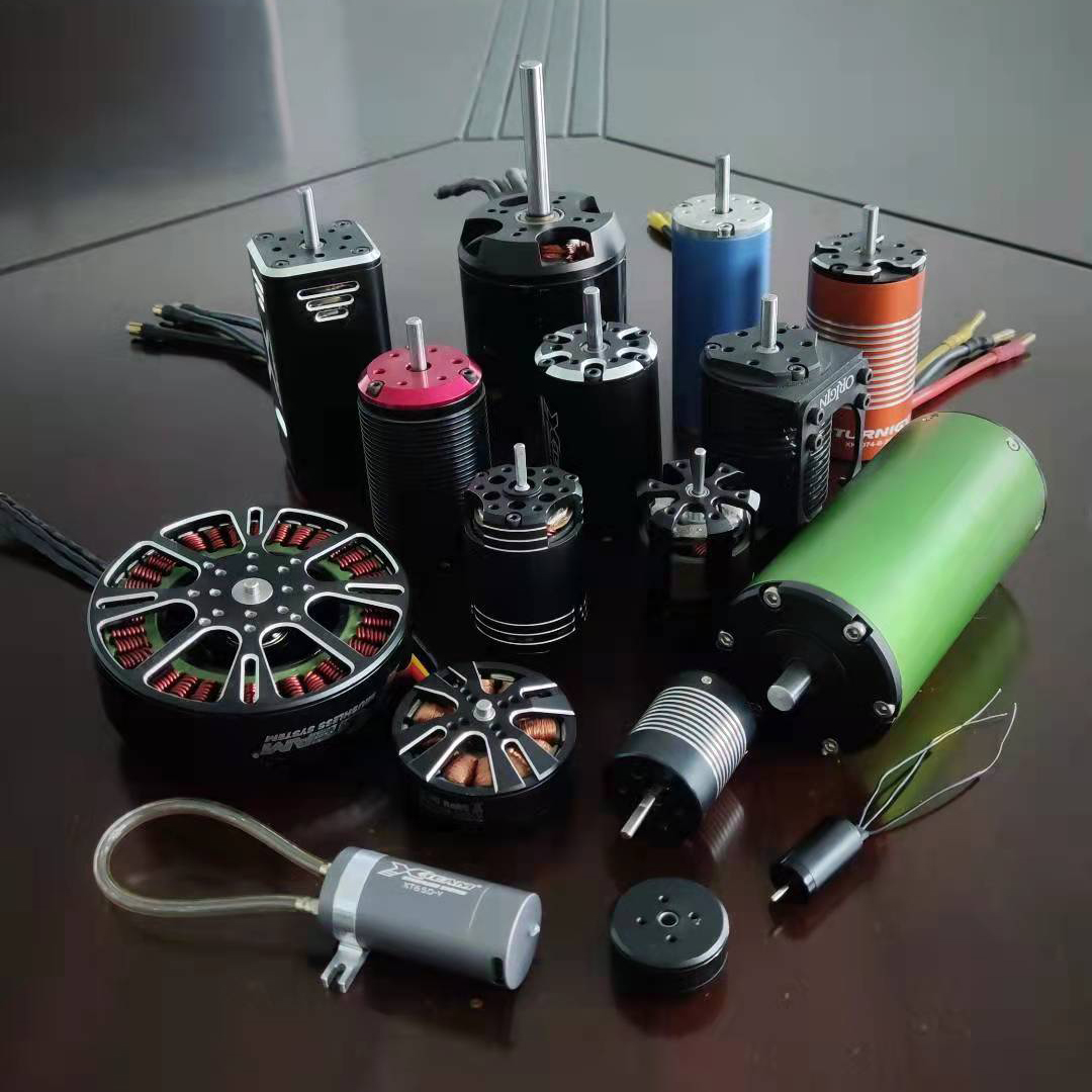 Collection of brushless DC motors and related components laid out on a table, including cylindrical can motors, stators, and a green power unit, for RC or industrial use.